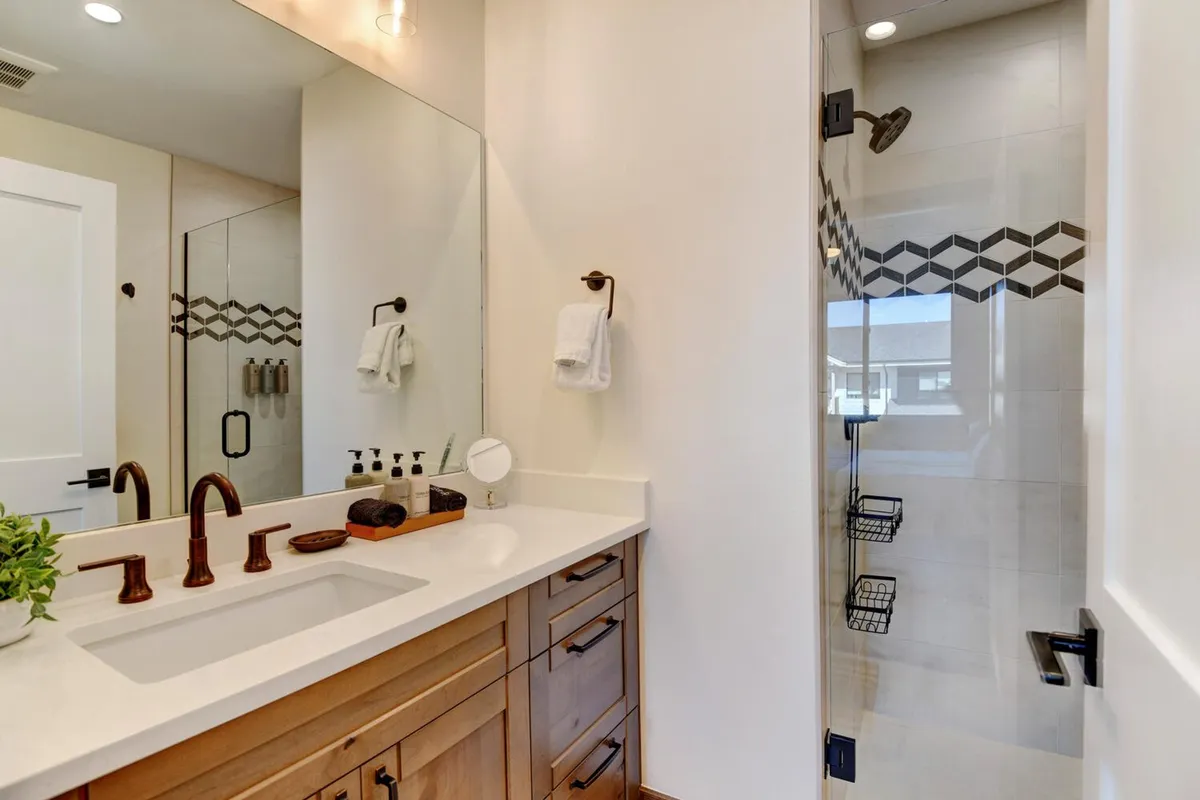 This bathroom image highlights a modern vanity with a sink, walk-in shower with decorative tile patterns, and clean, refreshing aesthetics. The space looks calm, bright, and spa-inspired, emphasizing comfort and luxury.