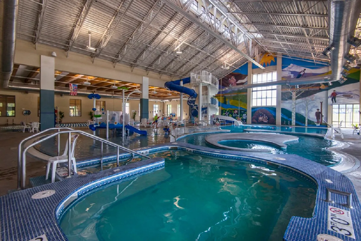 A vibrant indoor pool and water slides, with children and families playing. Colorful murals and the lively atmosphere evoke the spirit of daily fun and accessible recreation, reminiscent of the Grand Park Rec Center and family-friendly activities nearby.
