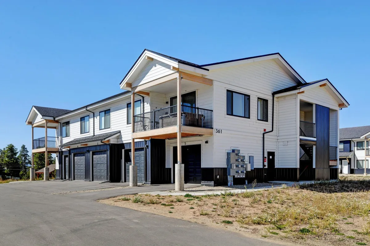 This image shows the main entrance to the condo, featuring the welcoming balcony and visible garage doors. The exterior portrays a modern, inviting entryway with mailboxes and a hint of neighboring community life, suggesting easy access and convenience for arrivals and departures. The included garage visually supports the mention of garage parking and additional exterior spaces.