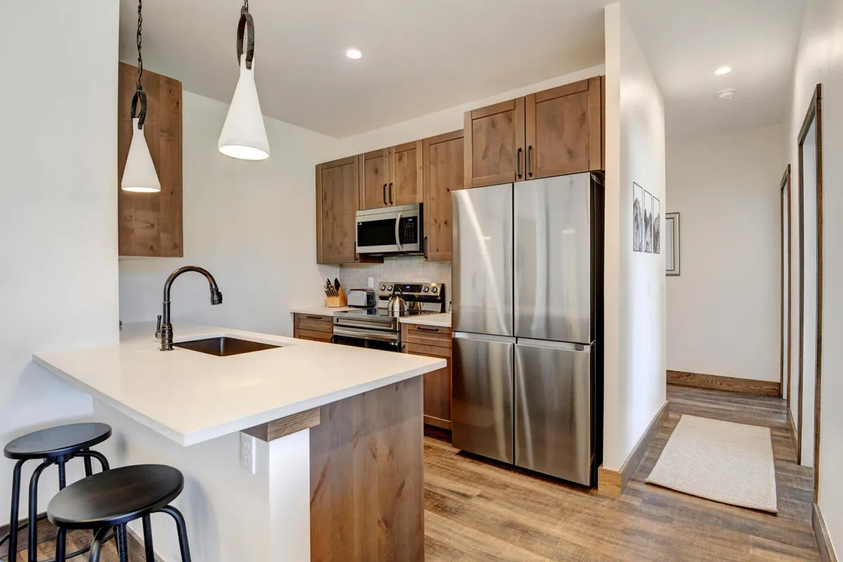 A beautifully appointed kitchen with a prominent island and bar seating, featuring stainless steel appliances, wood cabinetry, and elegant pendant lighting. The space is ready for cooking, socializing, and informal dining, capturing the gourmet, modern feel emphasized in the content.