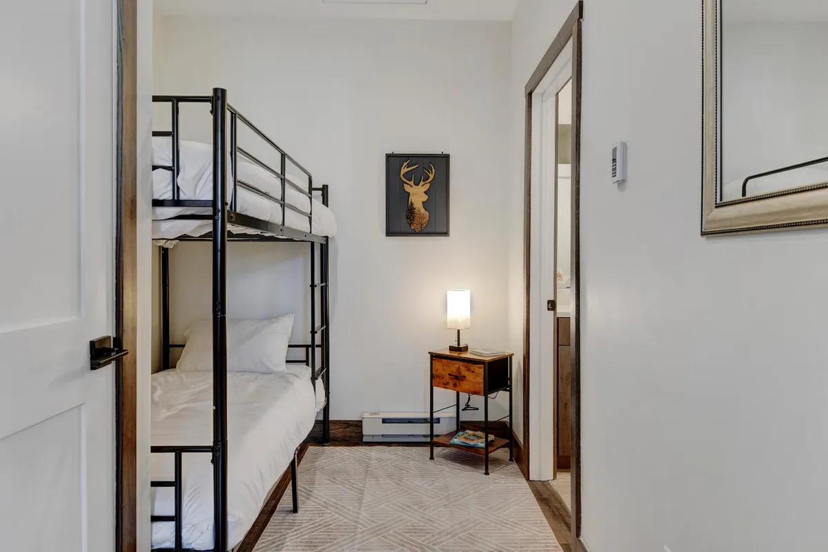 The image features a bunk bed setup with white bedding, playful artwork on the wall, and a nightstand with a lamp. The space feels inviting and whimsical—perfect for children or extra guests. The styling captures a fun and playful mood.